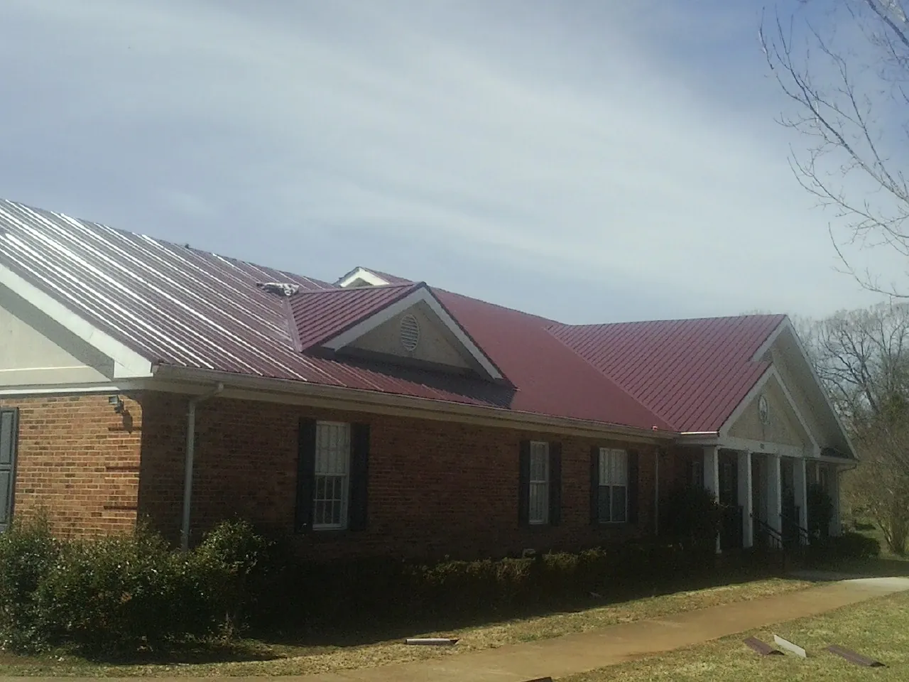 Red metal roof with gabled entries on a long brick building, from a Hail Damage Roof Repair job in Salineville