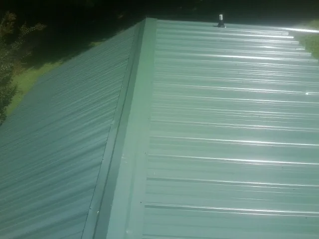 New green metal panels meeting at the ridge of a roof — Flat Roof Repair work by our crew in Salineville