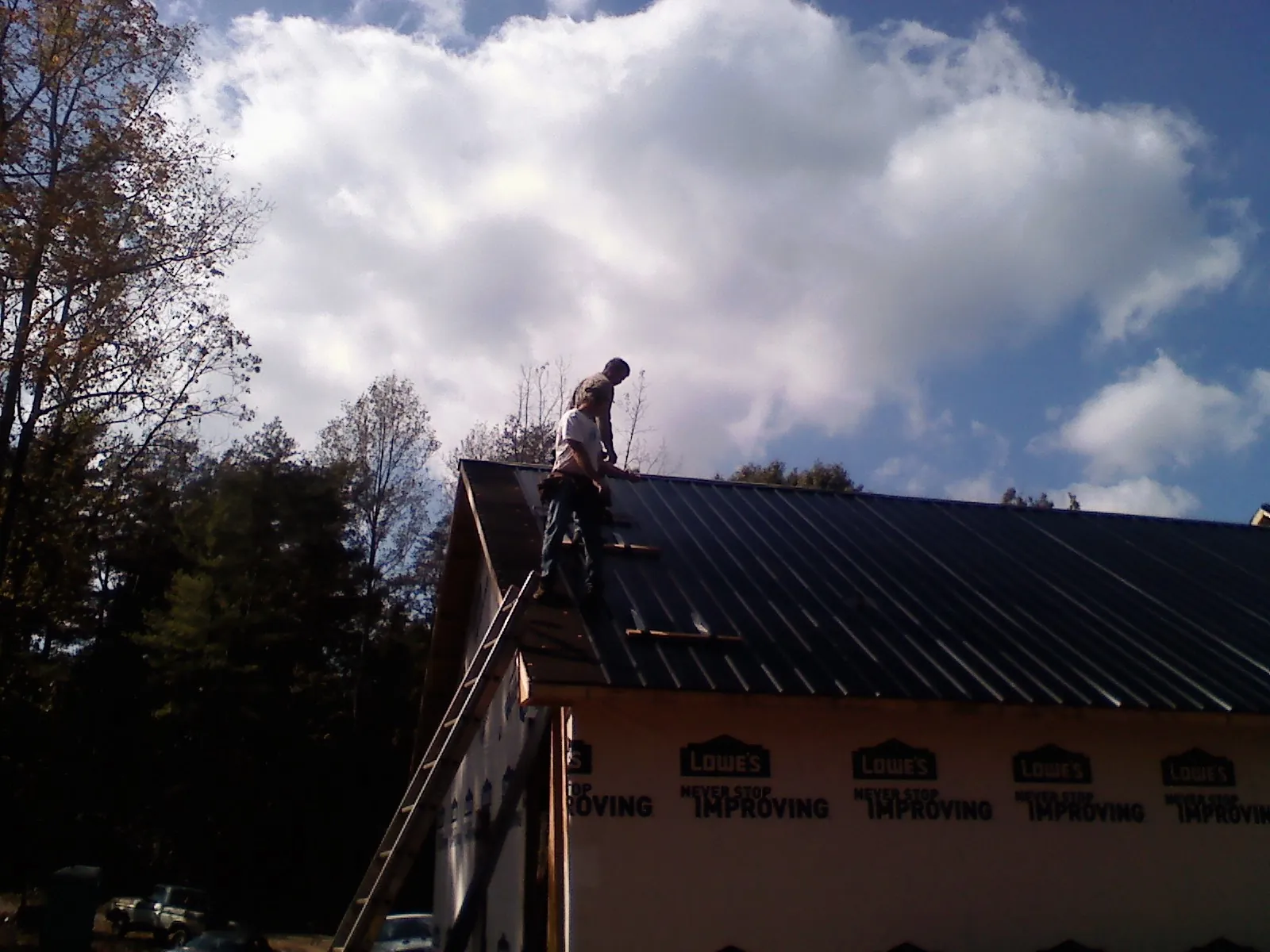 Roofer fastening dark metal panels high against a cloudy sky, from a Roof Inspection job in Salineville
