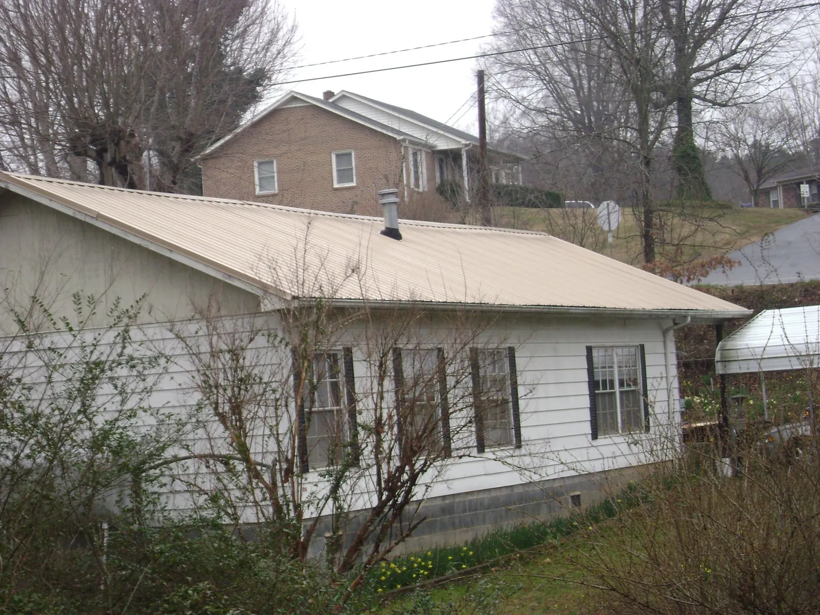 Tan metal roof on a white sided house set into a hillside — Commercial Roofing by Roofing Brothers in Salineville
